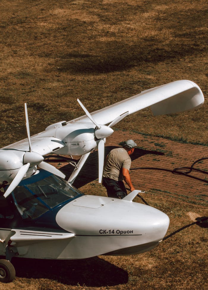 Services A man is standing beside an aircraft on a grassy field. Overhead shot.
